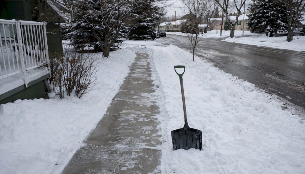 Partially shoveled Calgary sidewalk with snow shovel