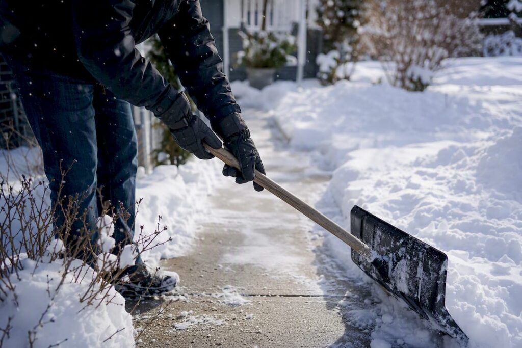 Hands shoveling snow on Calgary sidewalk
