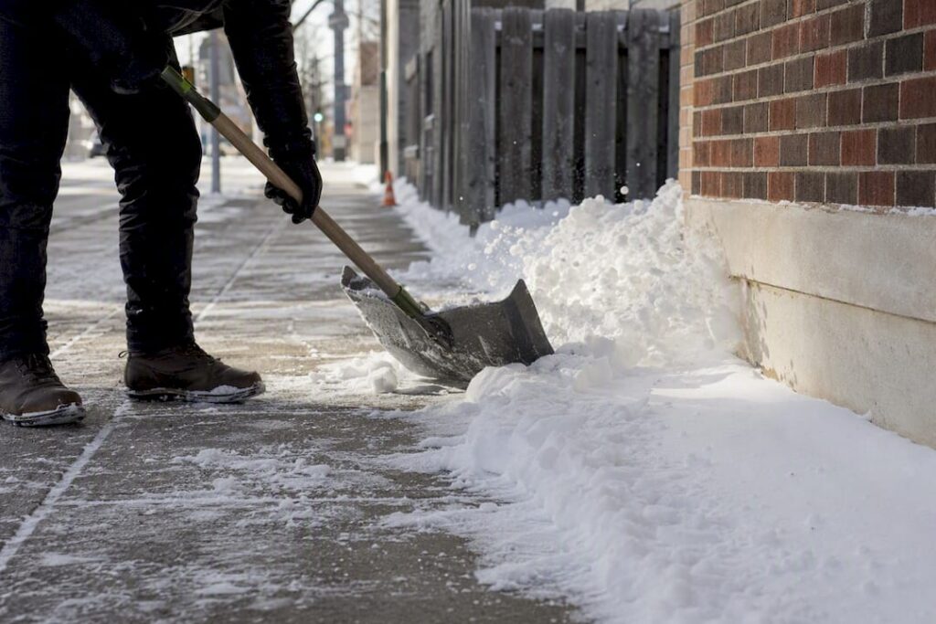 Gloved hands shoveling snow from sidewalk
